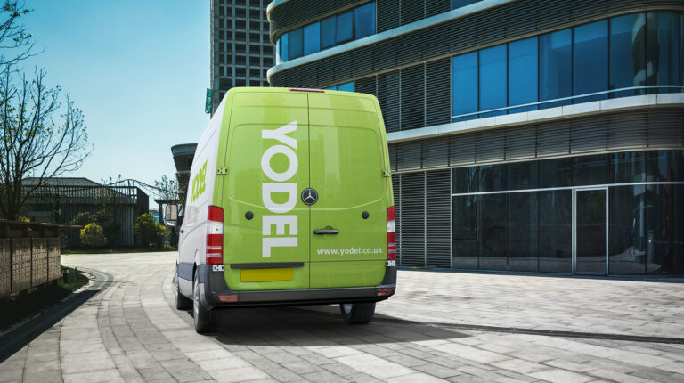 Back of Yodel van showing green and white logo in front of modern office building.