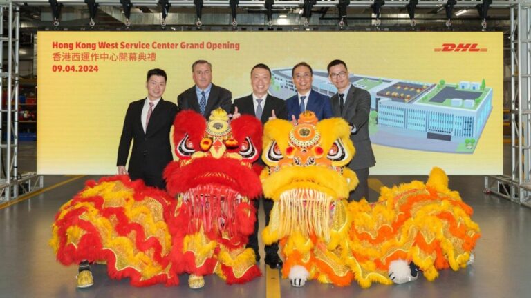 A group of five executives in suits stand in front of a screen that says "Hong Kong West Service Center Grand Opening", and behind two traditional Chinese festive dragon bulong props.