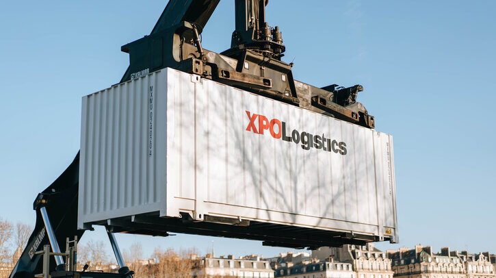 White XPO Logistics container being lifted by crane.