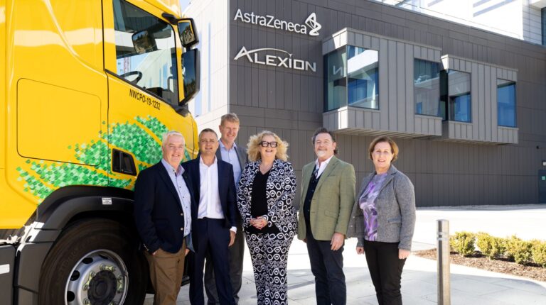 DHL Global Forwarding Freight Ireland and Alexion AstraZeneca Rare Disease standing in front of Alexion AstraZeneca Rare Disease headquarters with yellow DHL HVO truck in background