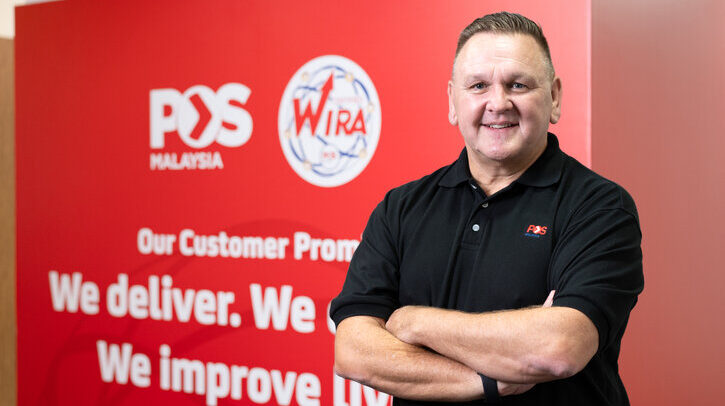 Charles Brewer, group CEO of Pos Malaysia in black shirt against red Pos Malaysia branded background
