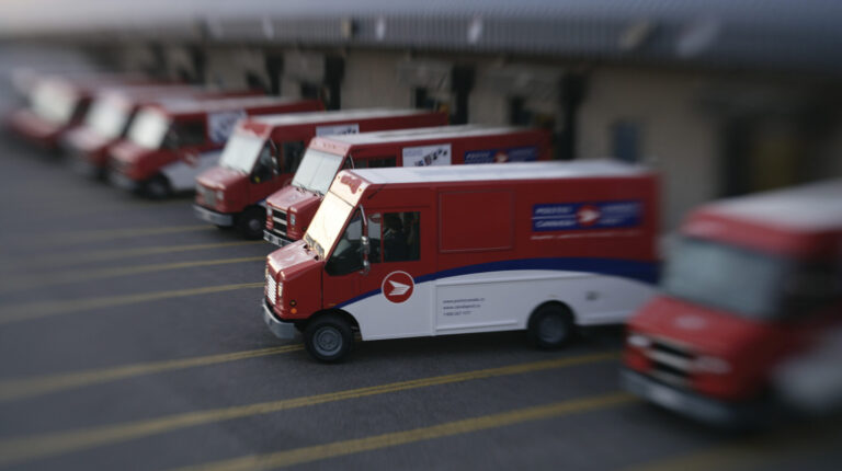 Row of Canada Post red post vans with one pulling out.