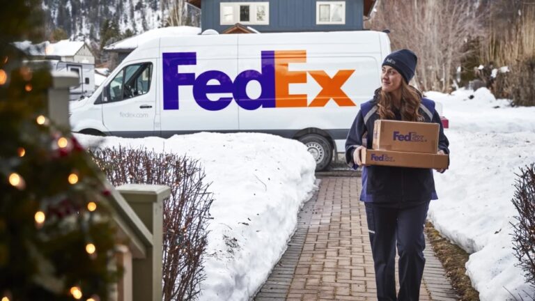 Female FedEx worker carrying parcel to the door with snow on the path and FedEx van in the background
