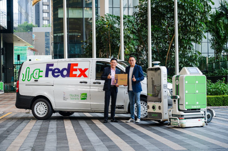 Two senior members of staff of FedEx and QuikBot stand in front of a FedEx delivery van and automation robots.