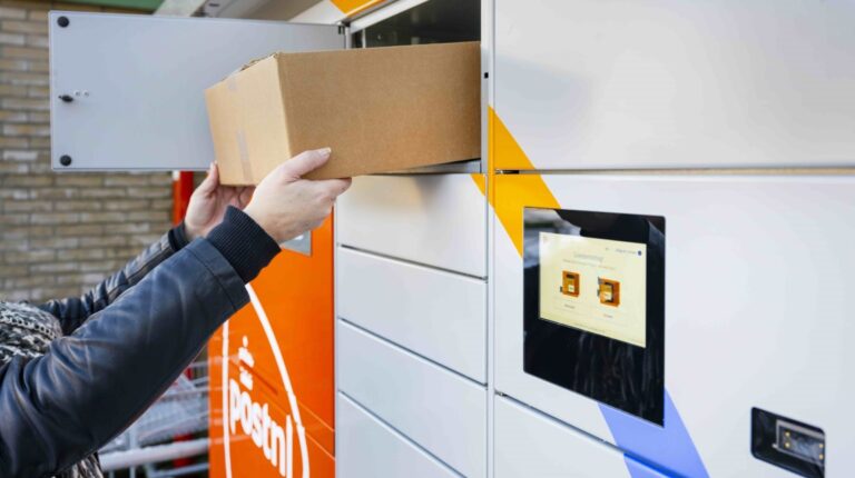 A person collects a brown box parcel from a locker in the top row of a a bank of PostNL lockers