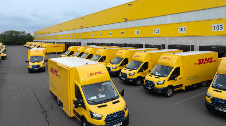 A row of yellow DHL trucks parked in a line outside a DHL facility