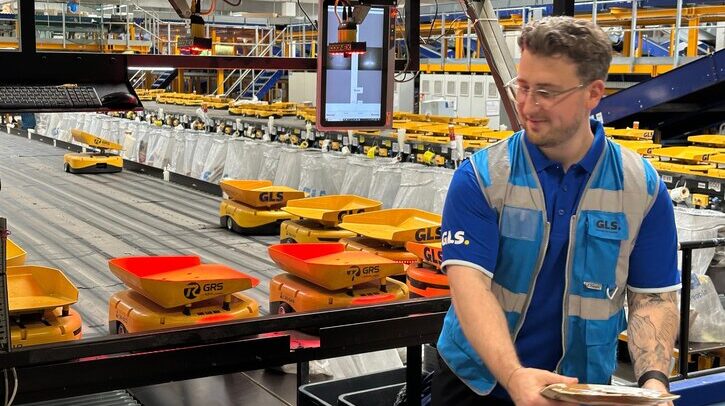 A GLS employee in a blue high-vis jacket working in a warehouse with a group of AGVs.