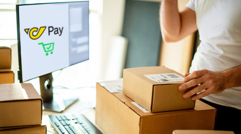 A peson at home using the PostPay service via a desktop coputer with two e-commerce delivery brown boxes in front of them