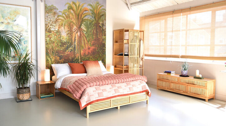 A futon bed with a terracotta cover in a bright bedroom with windows with open blinds