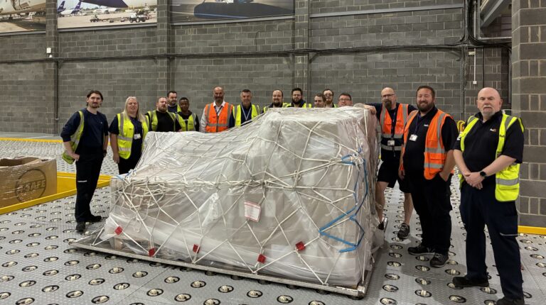 FedEx staff stand inside the new freight facility at East Midlands Airport in the UK, with pictures of FedEx aircraft on the wall behind them