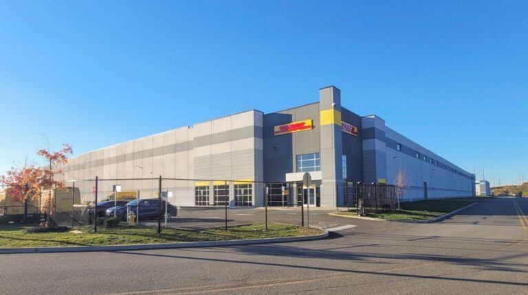 The exterior of a large DHL Express facility. There is a blue sky above