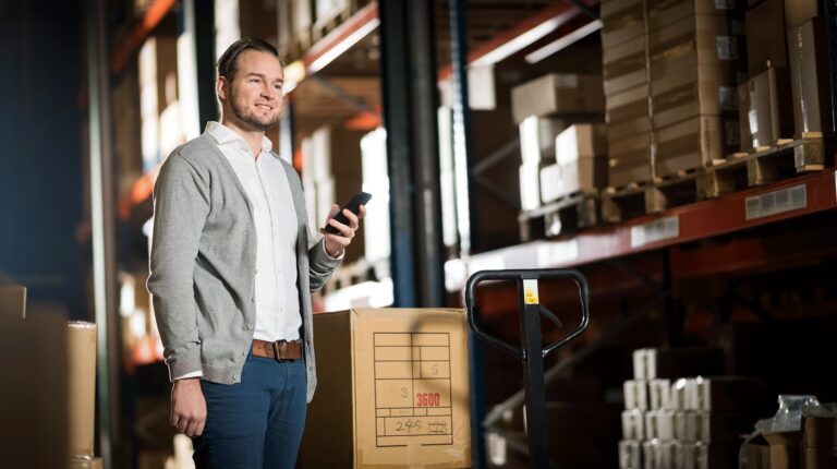 A PostNL worker stands in a fulfilment center holding a smart device