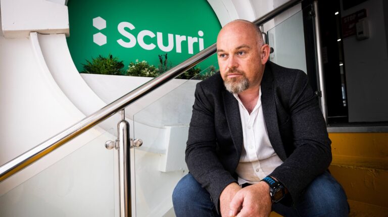 Scurri founder and CEO Rory O’Connor poses sat on a step in front of the company logo