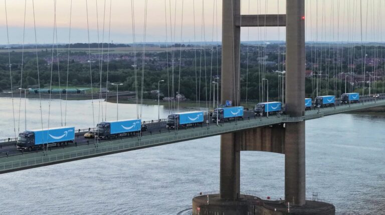 Blue Amazon trucks drive over a bridge in the UK