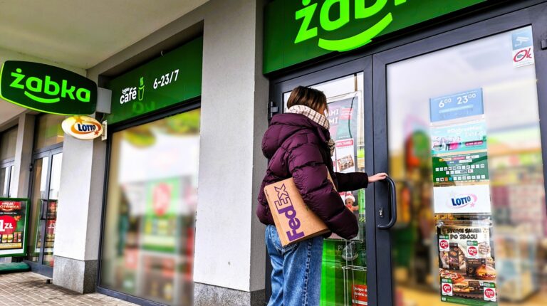 A custoemr walks into a Zabka convenient store. There is green branding above the door and the company name and logo in bright green